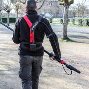 Person wearing a black and red Infaco backpack with a long pole in an outdoor setting.
