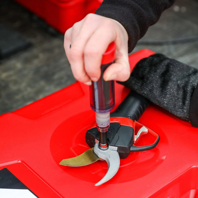 Person greasing electric shears on a surface.