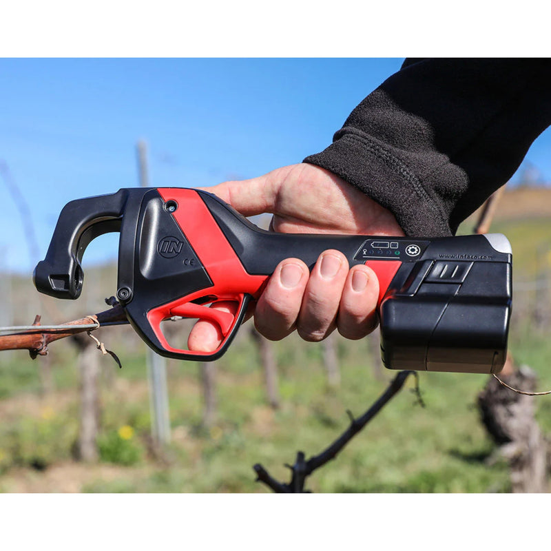 a person holding a red and black INFACO tool against a grape vine with blurred vineyard in the background