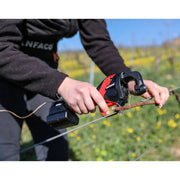a person holding a red and black INFACO tool against a grape vine with blurred vineyard in the background